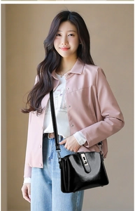 Detail of a black glossy crossbody bag with metal clasp styled with a casual outfit