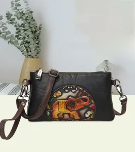 Detail of black pebbled leather crossbody bag with colorful embossed elephant design