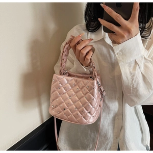 Detail of pink quilted bucket bag with rhinestones and woven handle on white linen