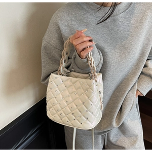 Detail of white quilted bucket bag with rhinestones and woven chain handle worn by model