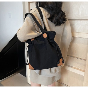 Vue détaillée du sac seau en toile noire avec garniture en cuir brun et cordon serrage