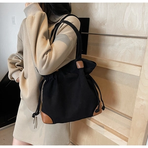 Détail du sac seau en nylon noir avec bordure en cuir marron porté par un mannequin femme