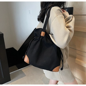 Sac seau minimaliste en nylon noir avec détails en cuir marron porté à l'épaule