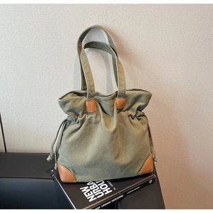 Detail of olive green canvas tote bag featuring brown leather trim and side drawstring