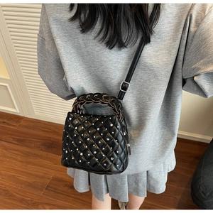 Detail of black quilted bag with silver studs and unique brown woven cylinder handle