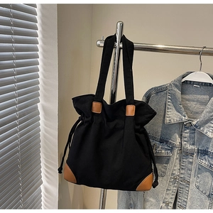 Détail d'un sac cabas en toile noire avec fermeture à cordon et coins en cuir brun