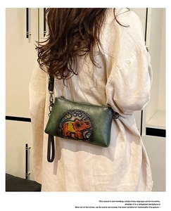 Detail of dark green leather envelope bag with embossed elephant art and brown strap