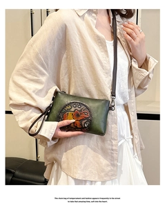 Detail of dark green leather envelope bag with elephant embossing and brown strap