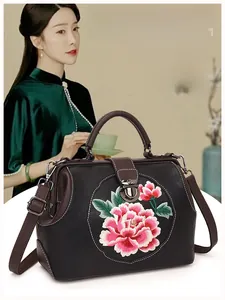 Close-up of pink peony embroidery on brown leather bag with retro metal clasp