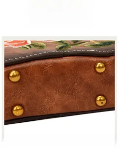 Detail of vintage brown leather handbag featuring golden bottom studs and floral embroidery