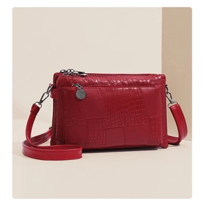 Detail view of red crocodile textured crossbody bag with multi-layer zippers and metallic charm