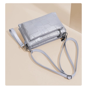 Detail view of silver crocodile embossed handbag featuring triple zipper compartments and strap