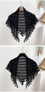 Détail d'un châle au crochet noir ajouré avec des glands à franges sur un cintre en bois