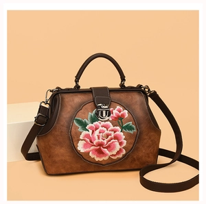 Macro detail of pink peony embroidery and metallic clasp on a brown vintage handbag