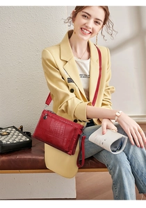 Detail of dark red crocodile texture envelope bag with silver zippers and crossbody strap