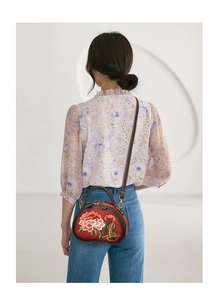 Detail view of ethnic red semi-round handbag with peony embroidery worn by model