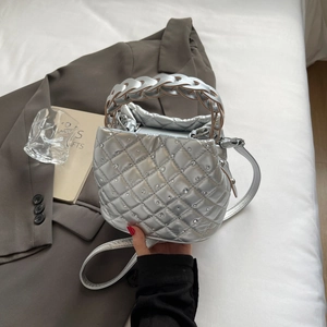 Silver quilted bucket bag with rhinestones and unique woven handle on grey blazer backdrop