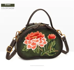 Close-up of pink peony floral embroidery and white stitching on green handbag