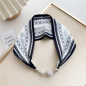 Detail of black and white silk scarf featuring geometric patterns and diamond-studded metal clasp