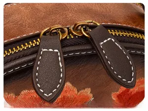 Close-up of golden dual zippers and floral embroidery on dark brown pebbled leather