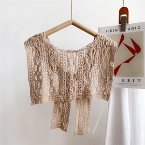Close-up of beige crochet lace shawl with intricate hollow patterns on a wooden hanger