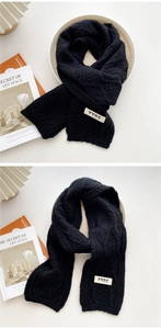 Detail of black cable knit scarf showing chunky texture and YYDS label on white surface