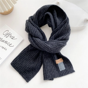 Close-up of dark grey knitted scarf with textured ribbing and brown leather brand label