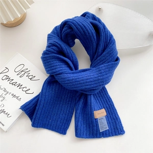Detail of royal blue knitted scarf featuring a brown leather logo tag and thick texture