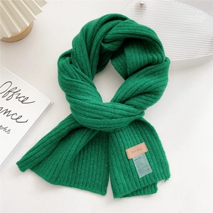 Close-up of emerald green chunky knit scarf with leather brand label on white background