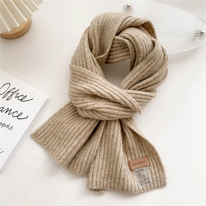 Detail of oatmeal knit scarf showing ribbed texture and leather logo tag on white background
