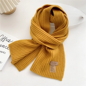 Detail of yellow ribbed knit scarf with leather brand tag on a clean white desk