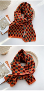 Detail eines orange-grünen Strickschals mit Karomuster, dicker Textur und Nahtetikett