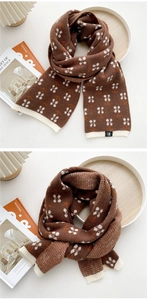 Detail eines kaffeebraunen Strickschals mit weißen Blumenmustern und Rippbündchen