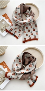Detail der cremefarbenen Strickschal mit rotem Kirschmuster und orangen Kontrastkanten