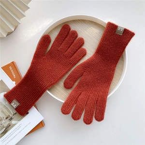Close-up of rust red knitted gloves with ribbed cuffs and leather brand label detail
