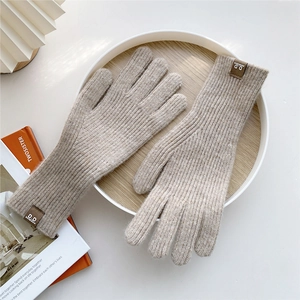 Close-up of oatmeal knitted gloves with leather brand label on a wooden tray
