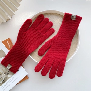 Detail of red cable knit winter gloves with ribbed texture and circular letter patch