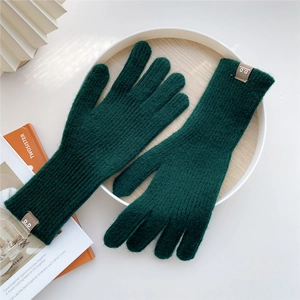 Close-up of forest green knitted gloves with ribbed cuffs and a leather label on wood