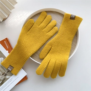 Detail of yellow knit wool glove with ribbed texture and brown leather brand label