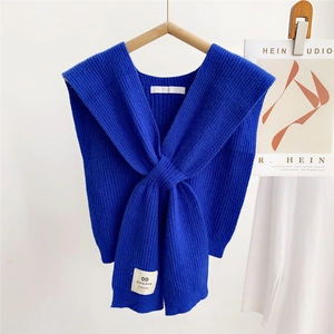 Detail of royal blue knitted shawl featuring a ribbed cross knot design and woven brand label