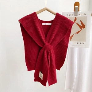 Close-up of a red knitted shawl with chunky texture and elegant cross-over knot design