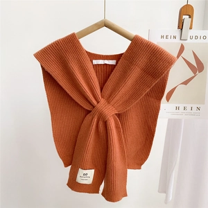 Detailed knit texture of an orange knitted crossover shawl with a white woven label