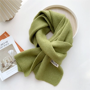 Detail of green ribbed knit scarf featuring a white woven GRACE logo label on the edge