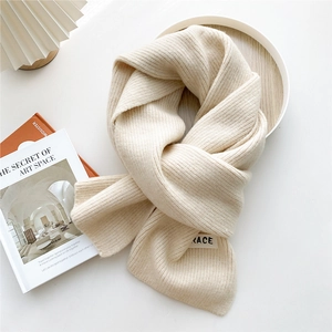 Detail of chunky knit beige scarf with a minimalist ACE letter label and soft ribbed texture
