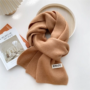 Close-up of khaki ribbed knit scarf with GRACE label on a minimalist aesthetic tray