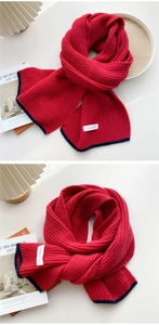 Close-up of thick red knit scarf with navy trim and brand label in cozy setting