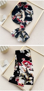 Detail of elegant black silk scarf featuring vibrant red and pink floral print in a bow style