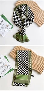 Detail of checkered long silk scarf with green edges tied on a wooden display board