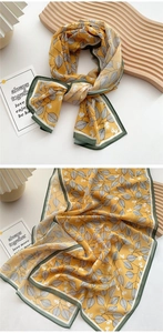Detail of a bright yellow silk scarf with white leaf patterns and a green stitched edge