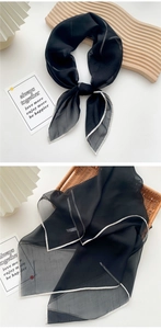 Detail of thin black chiffon scarf with grey edges tied as a bow and folded in a basket